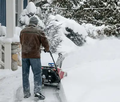 Residential snow removal technician using a snow blower to clear a home driveway and walkway in Chicago, IL