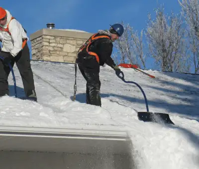 Professional technicians performing roof snow removal with safety harnesses and shovels in Chicago, IL
